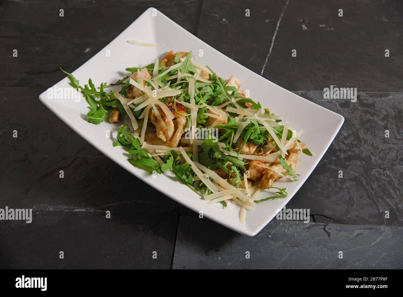 Pepite di pollo con bastoncini di formaggio e insalata di rucola su piatto bianco - shot studio orizzontale Foto Stock