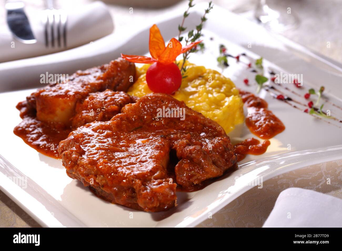 Manzo in salsa di pomodoro con risotto giallo e spezie su un piatto bianco in un ristorante. Foto Stock