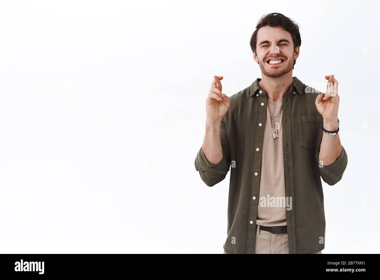 Eccitato ragazzo sorridente felice che fa desiderio, sogno ansioso venire vero, croce dita buona fortuna e chiudere gli occhi supplicare, vuole qualcosa accadere, anticipare Foto Stock