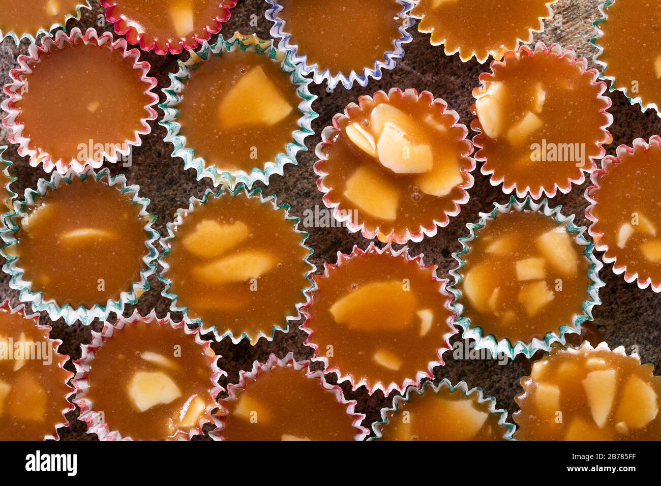 Caramelle al butterscotch svedesi knäck con mandorla, in piccole tazzine di carta multicolore. Primo piano su una superficie di pietra grigia. Visto dall'alto, macro pho Foto Stock