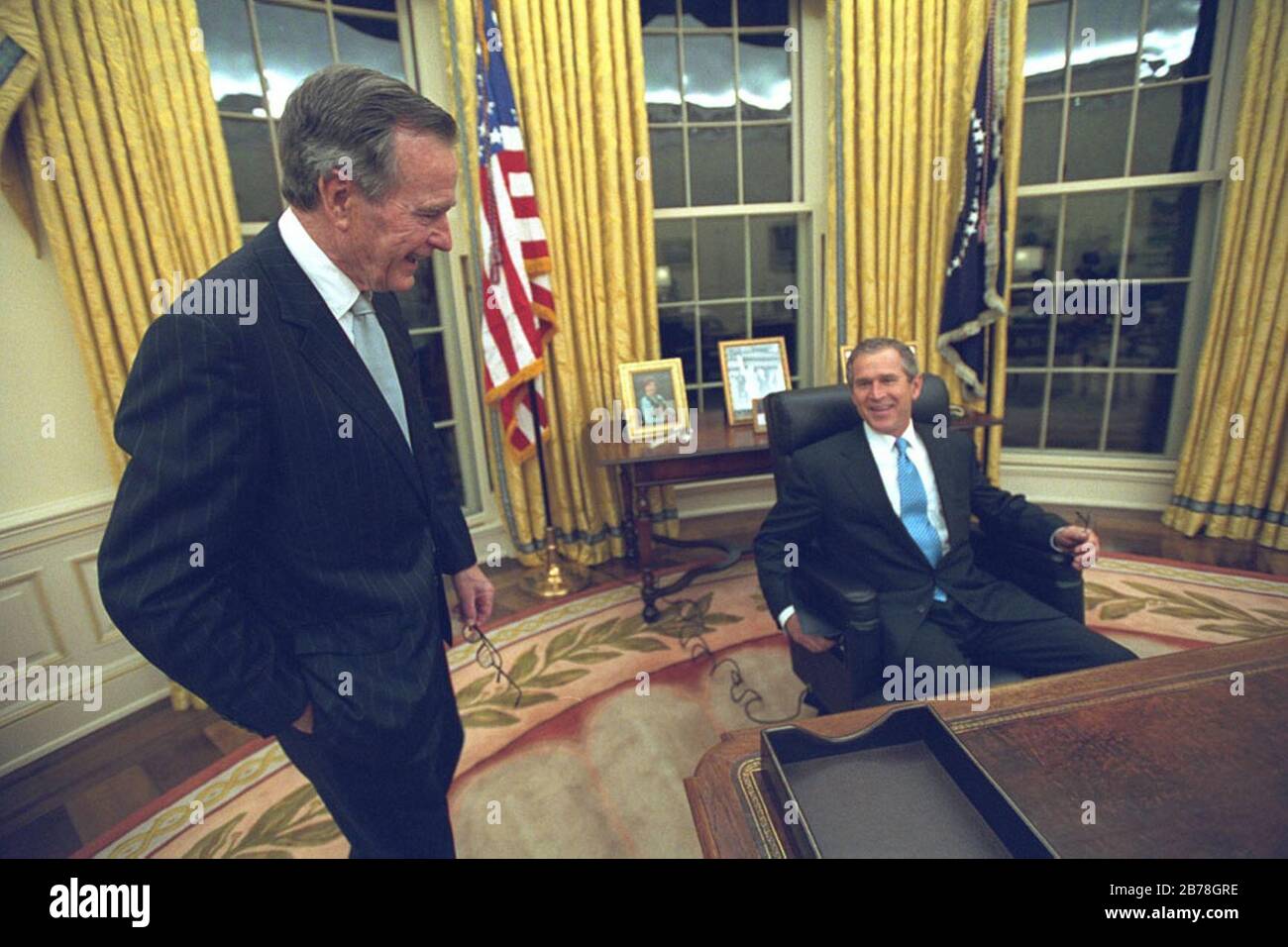 George W. Bush siede al Resolute Desk nell'Ufficio ovale mentre suo padre George H. W. Bush guarda sopra. Foto Stock