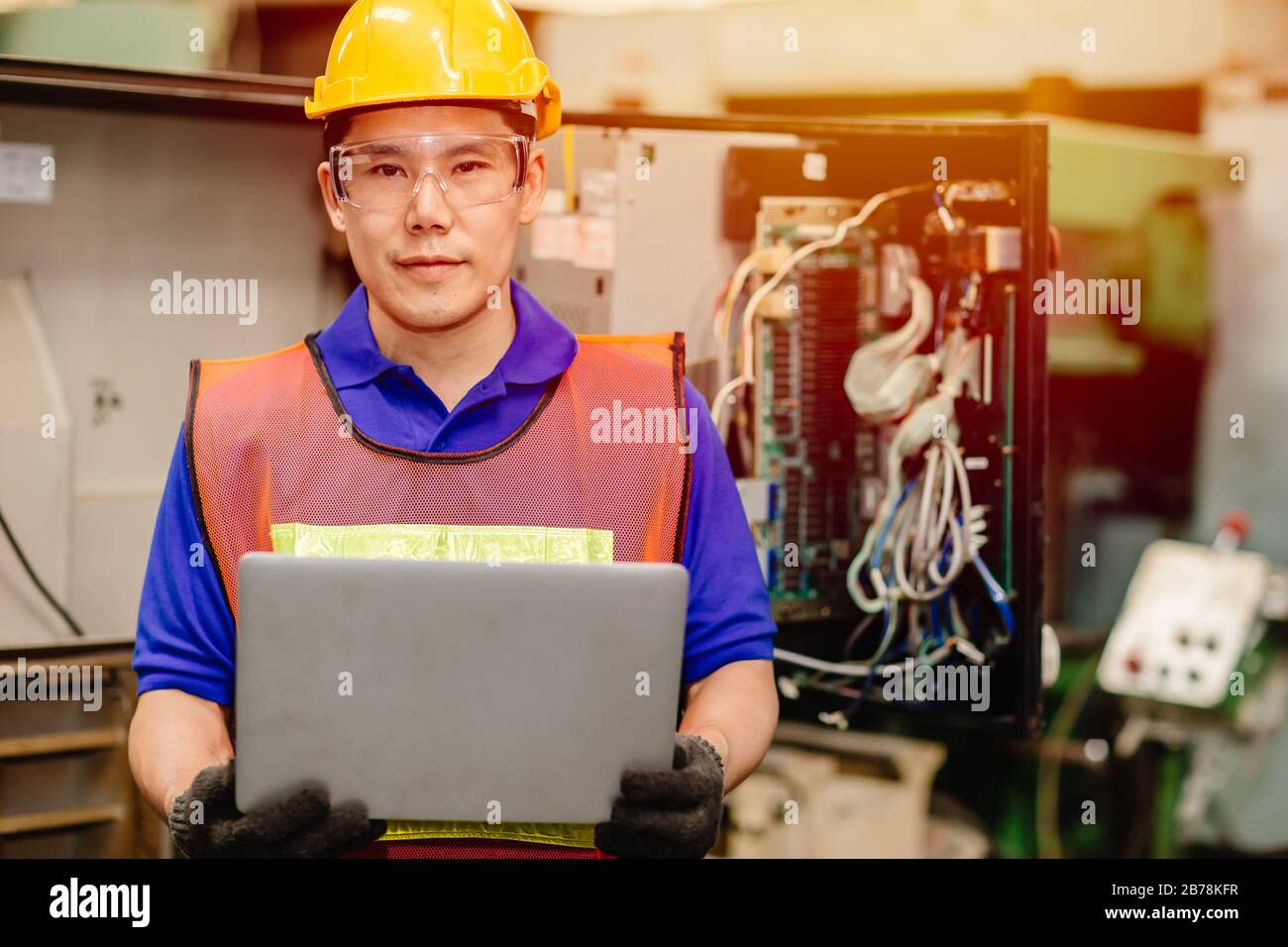 Ritratto del team di tecnici dell'assistenza che lavora con il pannello posteriore del cavo elettronico di una macchina industriale pesante per la riparazione e la riparazione di manutenzione con computer portatili Foto Stock