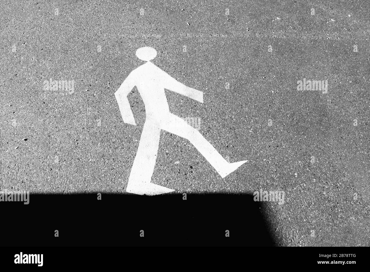 Cartello stradale sull'asfalto - uomo a piedi sul bordo dell'ombra. Foto Stock