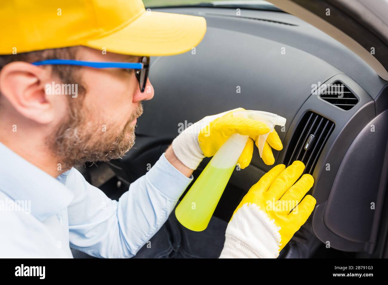 Uomo che pulisce il condotto d'aria della griglia di ventilazione dell'automobile e spruzza con il liquido di disinfezione. Foto Stock