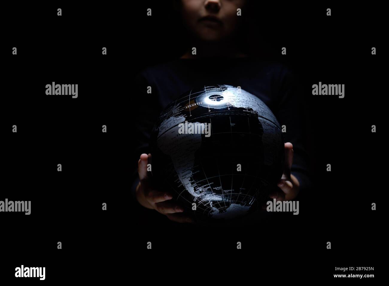 Mani di bambina che tiene mappa sfera globo isolato su sfondo nero. Malattia da infezione pandemica COVID-19. Inquinamento ambientale, ecologico Foto Stock