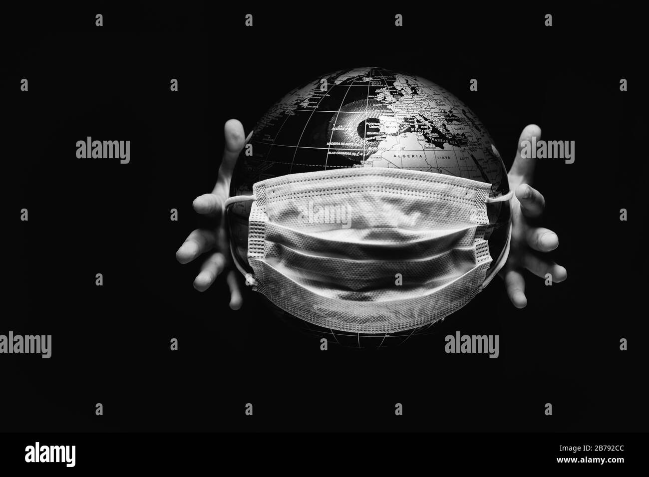 Mani di bambino piccolo che tiene sfera del globo, mappa del pianeta coperta con maschera protettiva medica isolata su sfondo nero. Concetto di pandemia COVID-19 Foto Stock