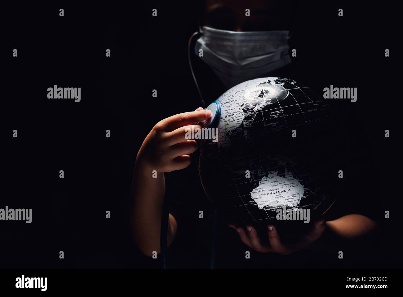 Mani di bambino tenere globo mettere stetoscopio sulla sfera ascoltare heartbeat, faccia coperta in maschera su sfondo nero. Problemi ecologici disastri e COVID- Foto Stock