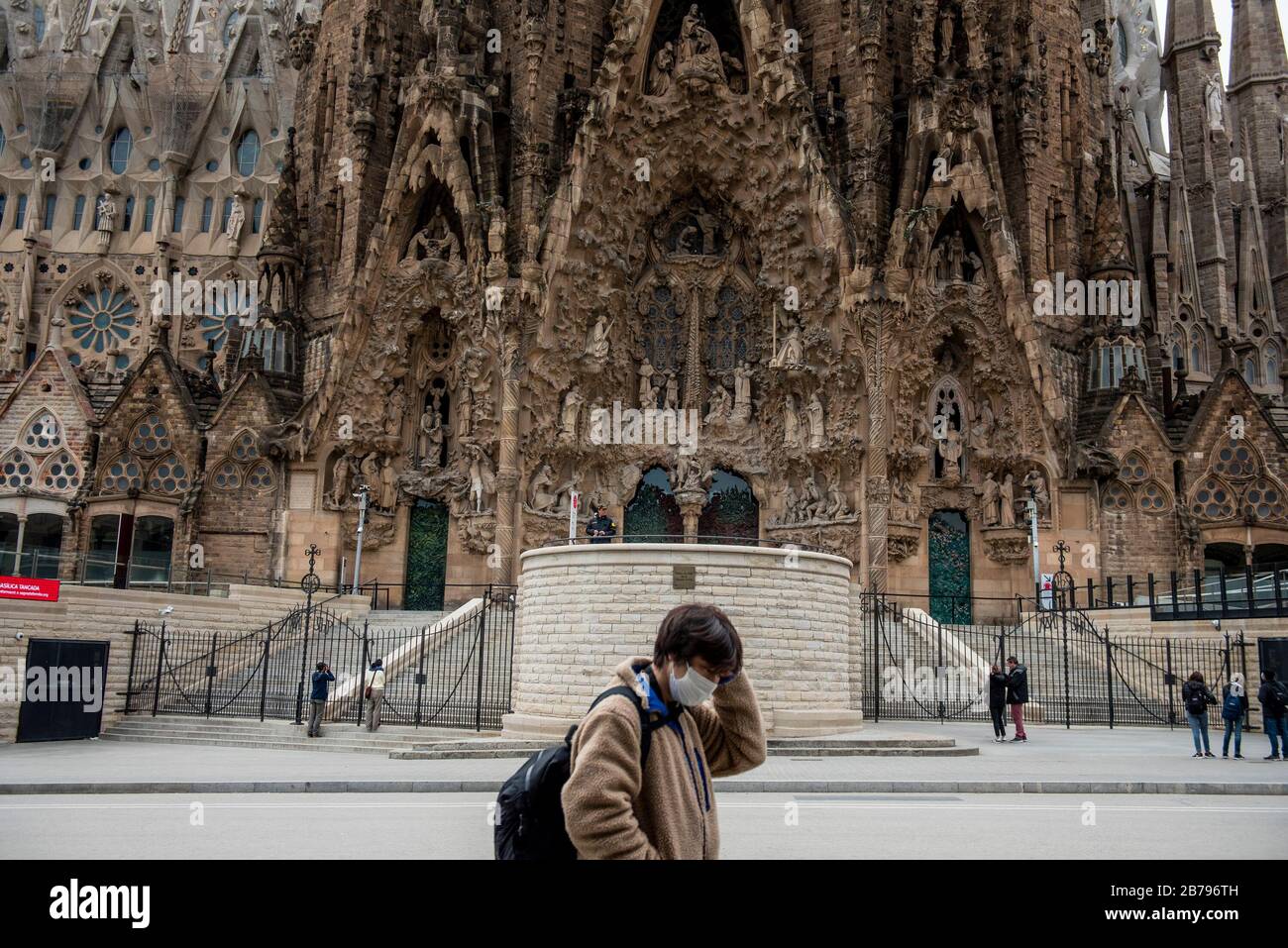 Un turista con una maschera come misura preventiva contro le passeggiate contro il virus della corona passò la Basilica della Sagrada Familia durante il primo giorno dello stato di emergenza. Foto Stock