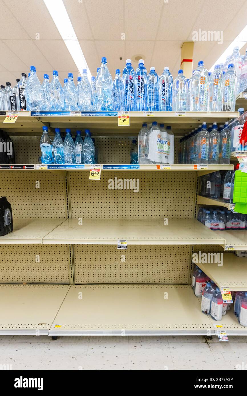 Scaffali quasi vuoti in un supermercato negozio di alimentari nel corridoio acqua in bottiglia come coronavirus causa paura e panico Foto Stock