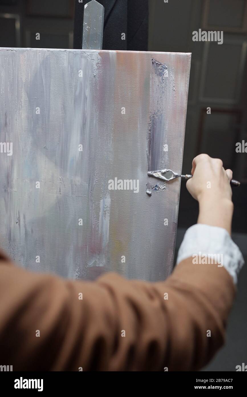 Mano di giovane artista femminile che utilizza uno strumento speciale per la pittura mentre si applica la vernice grigio argento sulla carta durante il lavoro in studio Foto Stock
