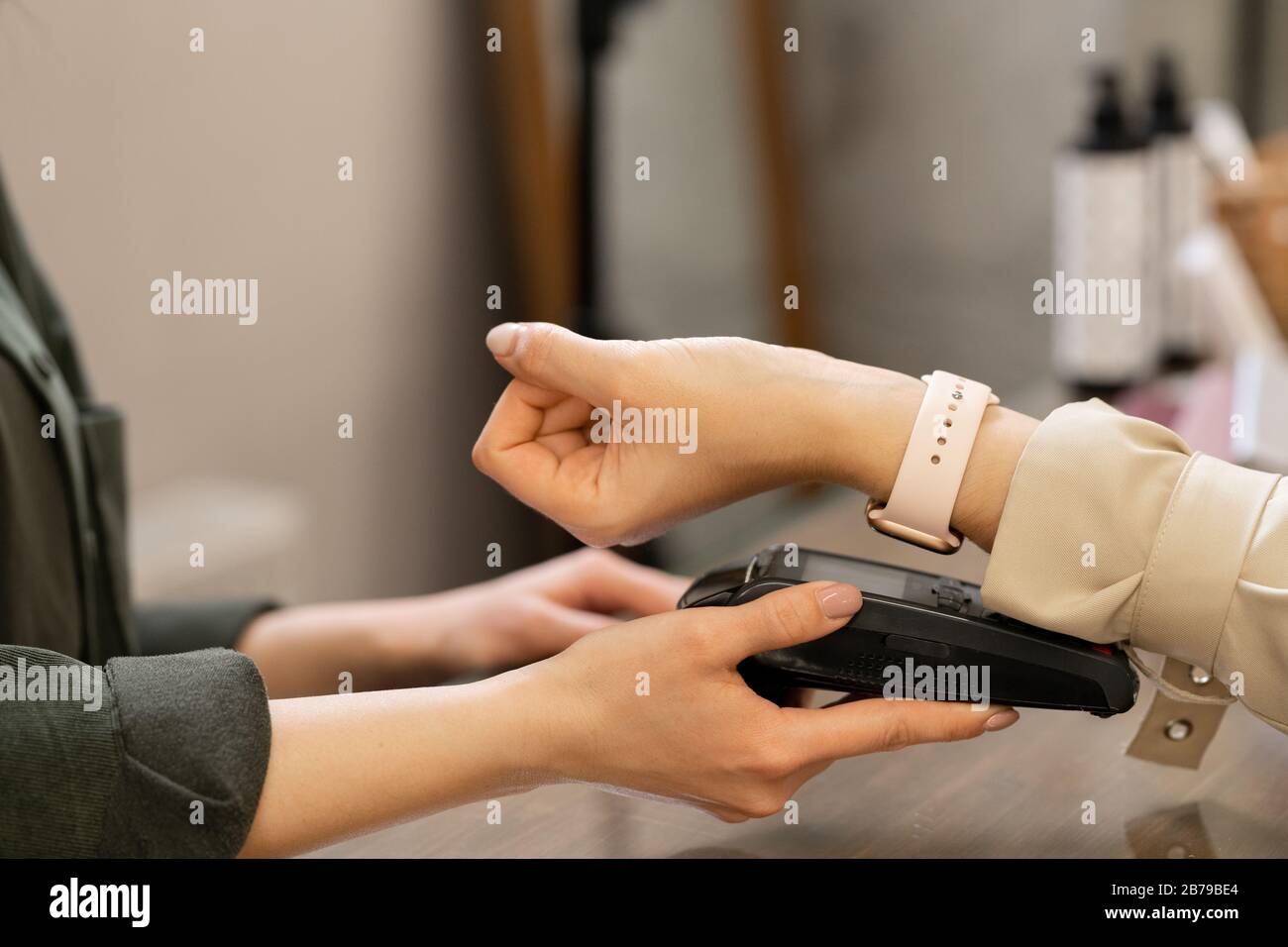 Mano di giovane cliente femminile contemporaneo con smartwatch che tiene il polso sul terminale pos durante il pagamento senza contatto Foto Stock