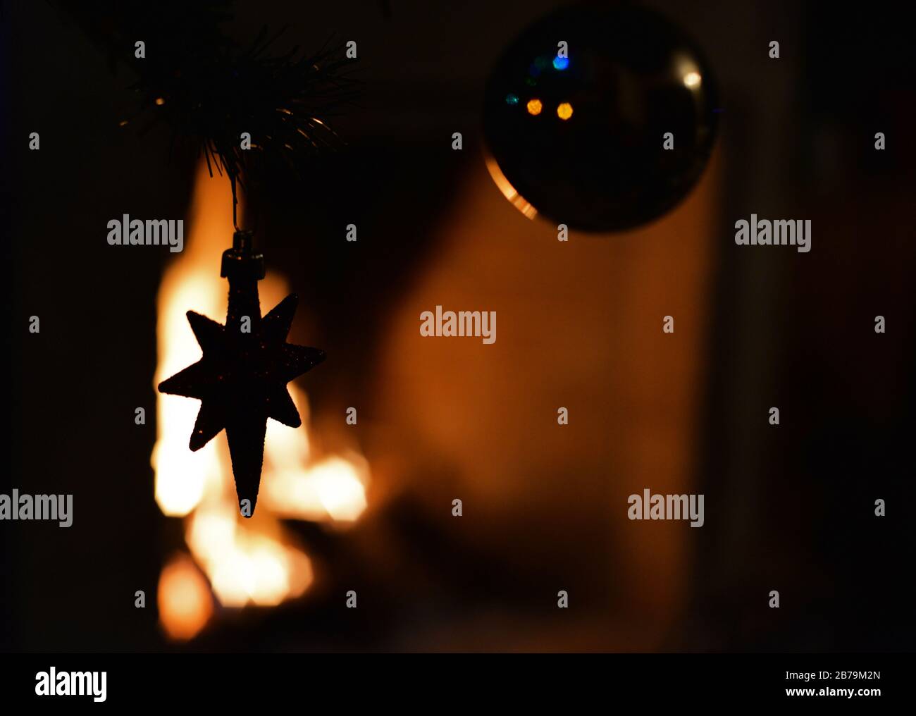 Stella decorativa appesa ad un albero di Natale contro l'illuminazione di un camino. Concetto: Stagione festiva. Foto Stock