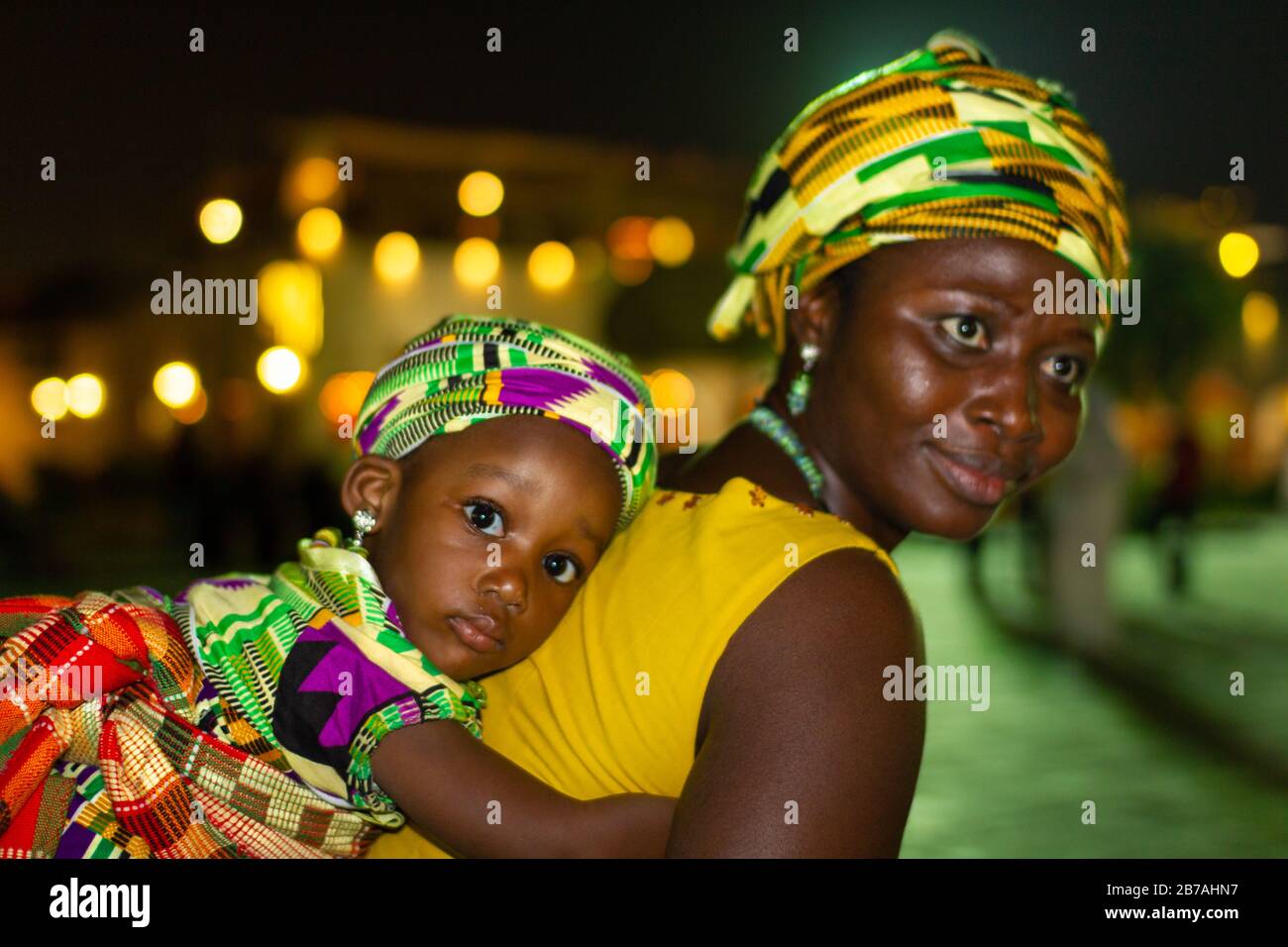 Madre africana che porta sua figlia sulla sua schiena in costumi tradizionali tribù africane con sfondo sfocato Foto Stock