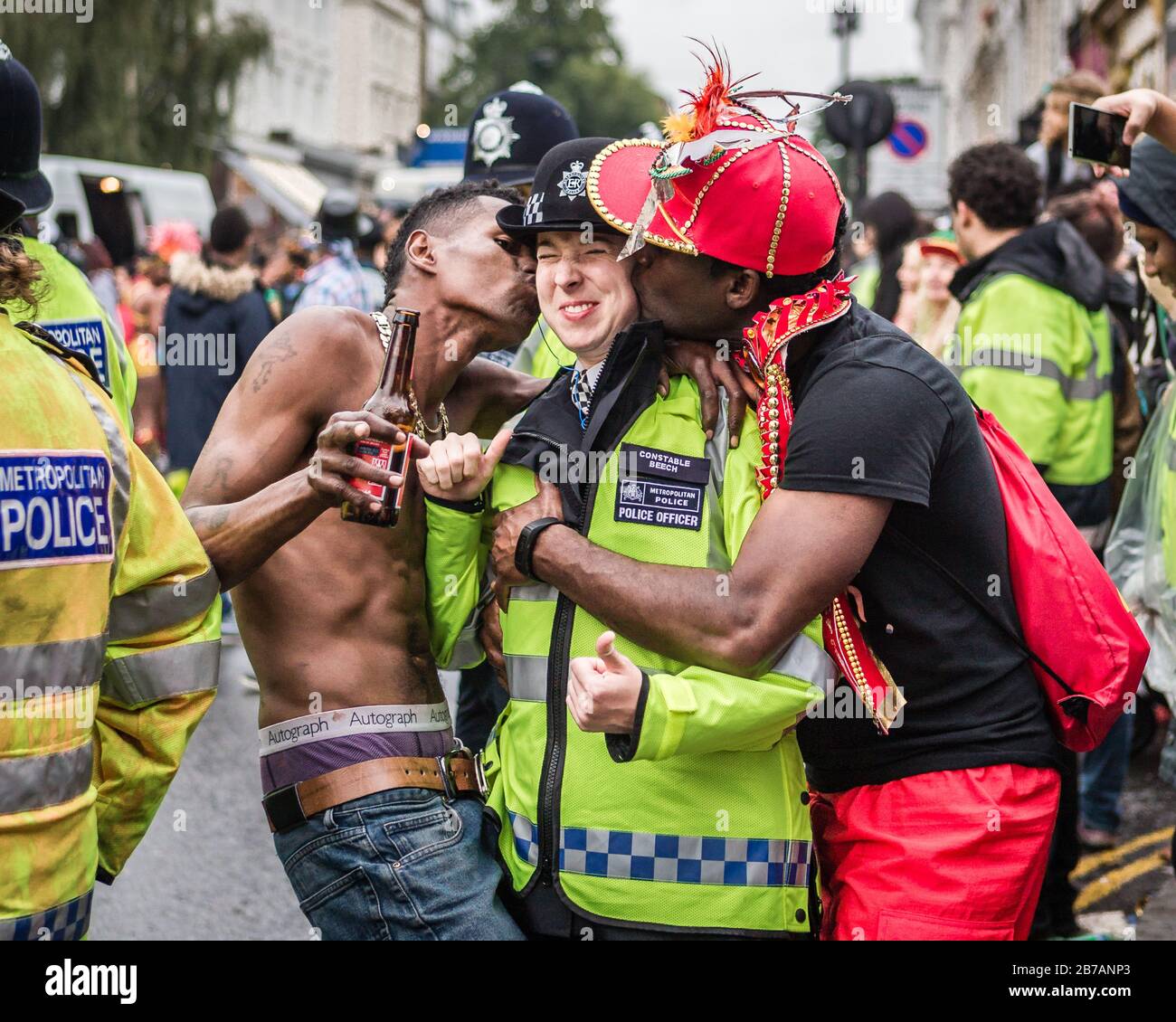 Due rivelatori piantano un bacio allegro su un poliziotto mentre dà i pollici al Carnevale di Nottinghill a Londra. Foto Stock