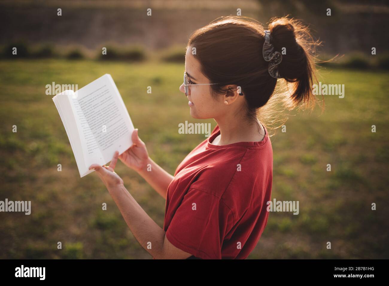 Giovane donna che ha una bella lettura mentre sorridente e godendo la luce di un tramonto in un parco. Foto Stock