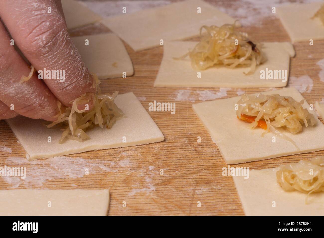 Una donna scolpisce gnocchi e ravioli da quadrati di pasta e cavolo. Pannello di taglio compensato, setaccio di farina di legno e perno di laminazione di legno - attrezzi per Foto Stock