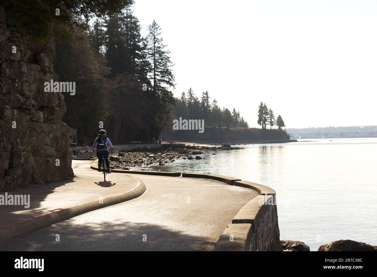 Vancouver, Canada - 21 febbraio 2020: Una donna sta cavalcando sul sentiero del muro di mare vicino alla terza spiaggia nello Stanley Park durante la bella giornata di sole Foto Stock