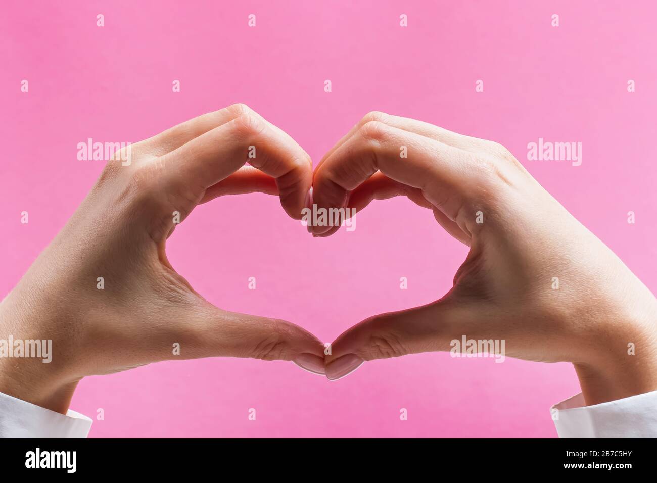 Mani femminili che formano un simbolo del cuore su sfondo rosa Foto Stock