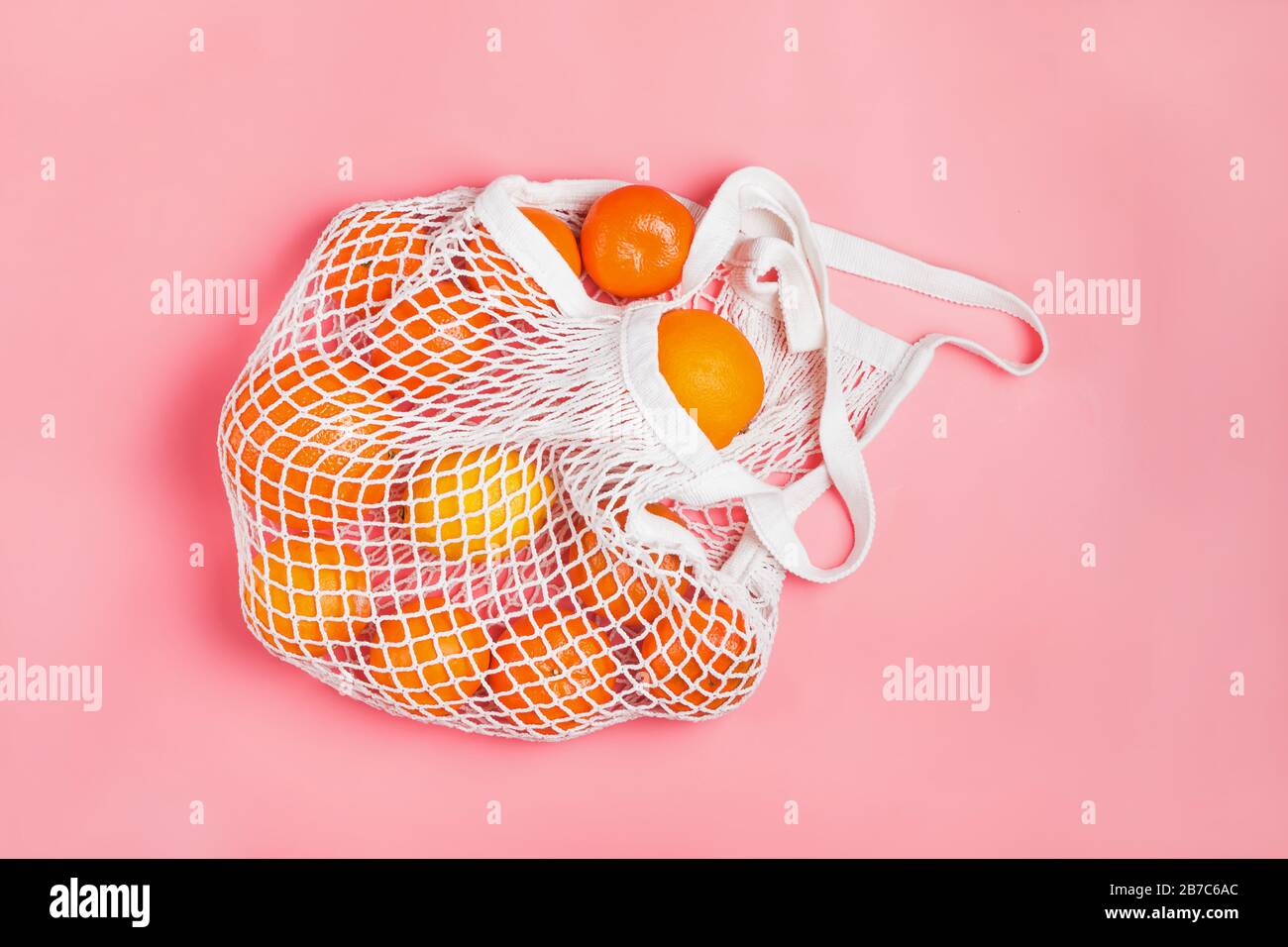 Borsa shopping in mesh con limoni e arance su sfondo rosa. Foto Stock