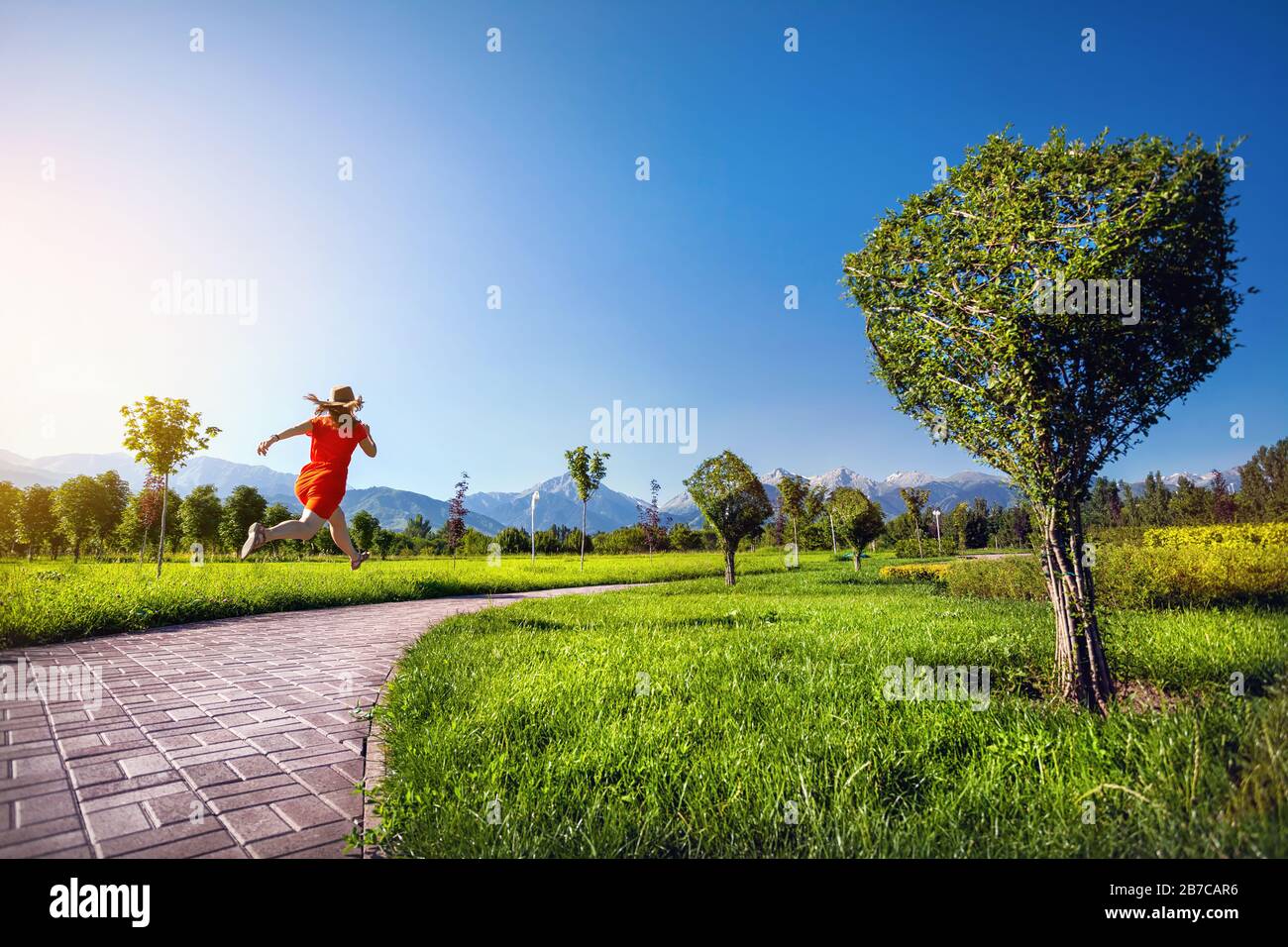 Donna in abito arancione che corre lungo la strada nel giardino di Topiary con alberi surreali a forma di cubo Foto Stock