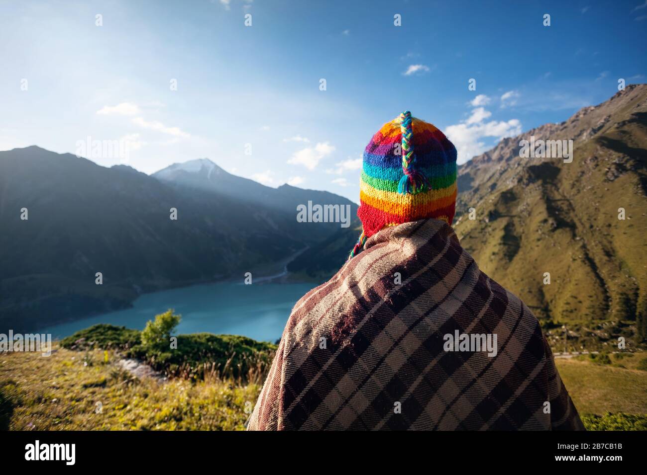 Donna turistica in cappello arcobaleno e poncho marrone godendo di una bella vista del lago Big Almaty in Kazakistan Foto Stock