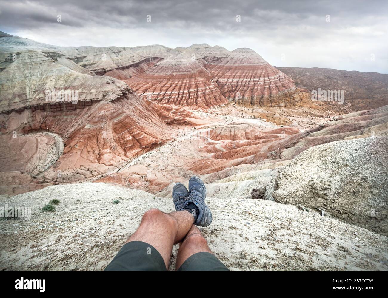 Gambe turistiche con scarpe grigie sulle Desert Mountains con strati rossi e bianchi su sfondo cielo nuvoloso Foto Stock