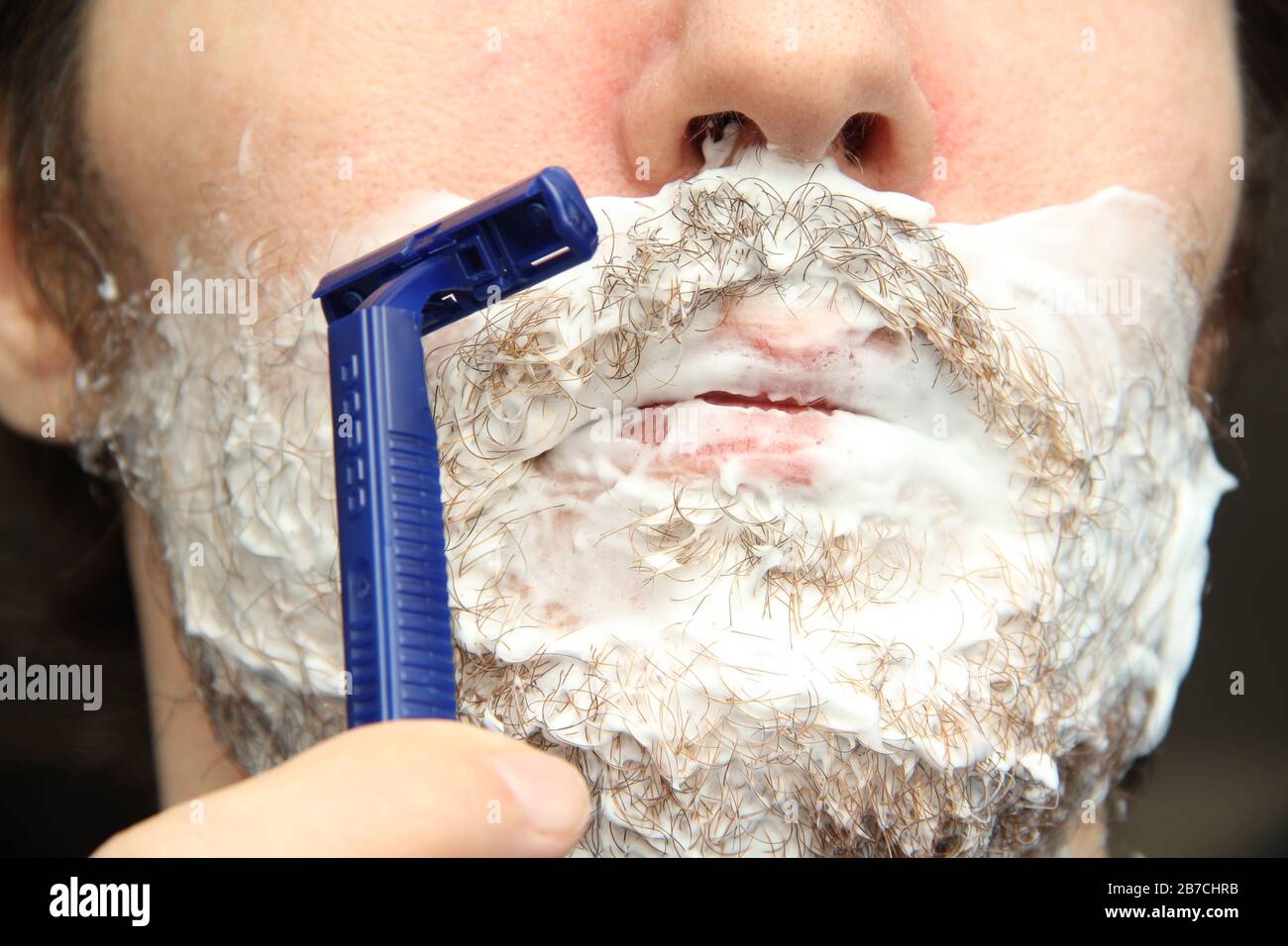 Un uomo rasa la barba con un rasoio di sicurezza monouso blu. Schiuma da  barba bianca sulle guance e sul mento Foto stock - Alamy