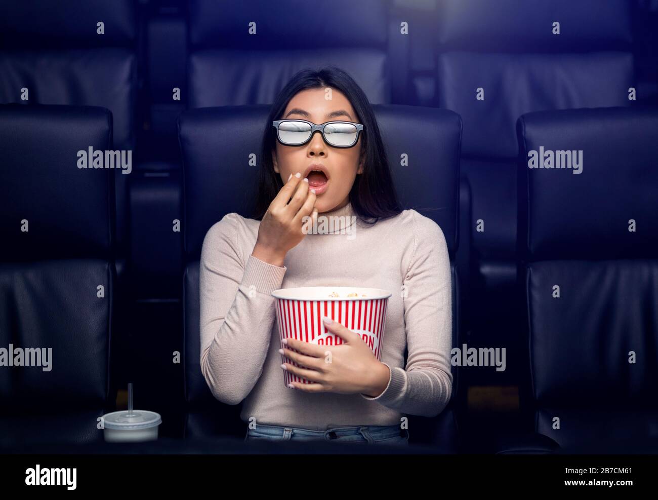 Andare ai film da soli. Donna asiatica spaventata in occhiali 3D guardando thriller al cinema Foto Stock