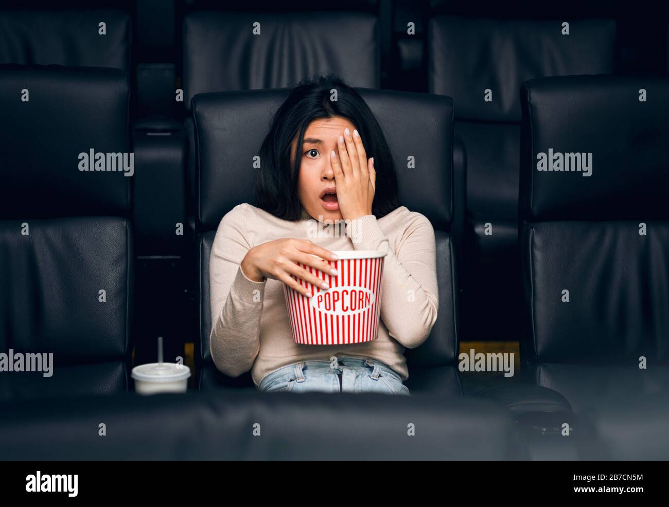 Giovane donna asiatica che chiude il suo viso nella paura sulla prima del film al cinema Foto Stock