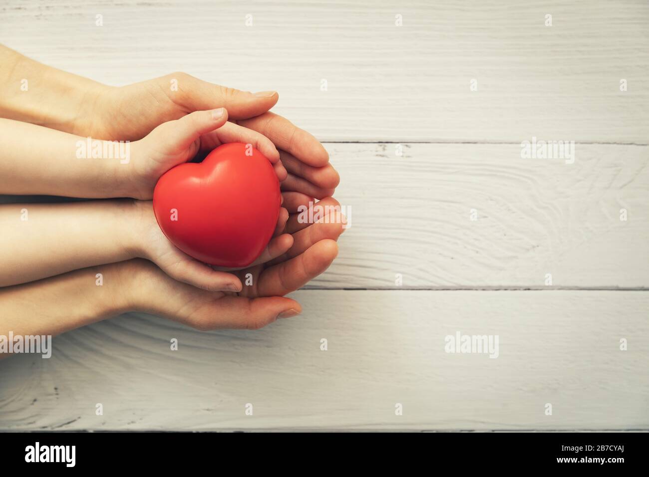 cuore rosso in mano bambino e adulto su sfondo bianco di legno. concetto di salute, donazione di organi, assicurazione famiglia Foto Stock