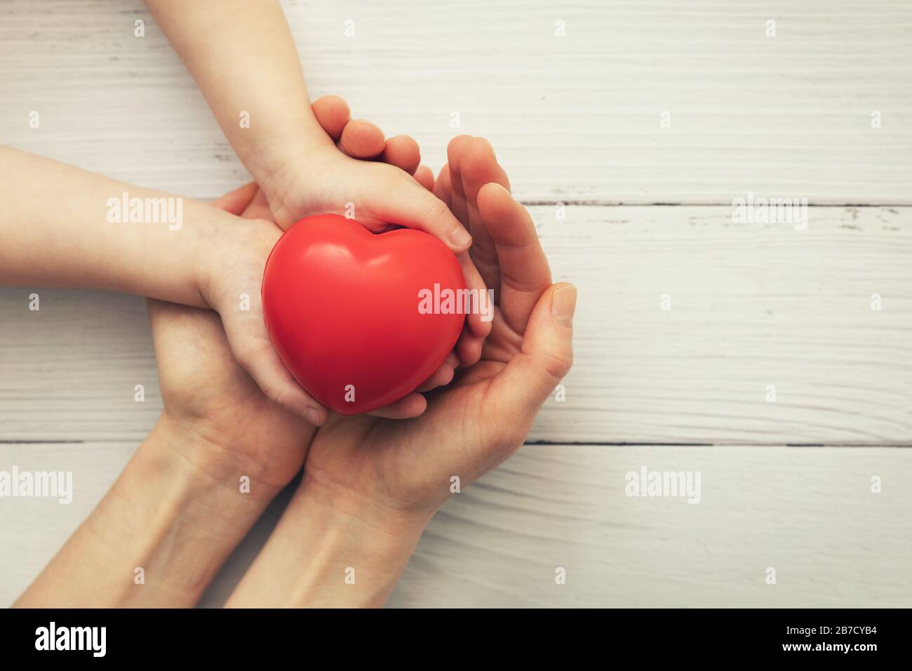 cuore rosso in bambino e madre passa su sfondo di legno bianco. concetto di amore, carità, empatia Foto Stock