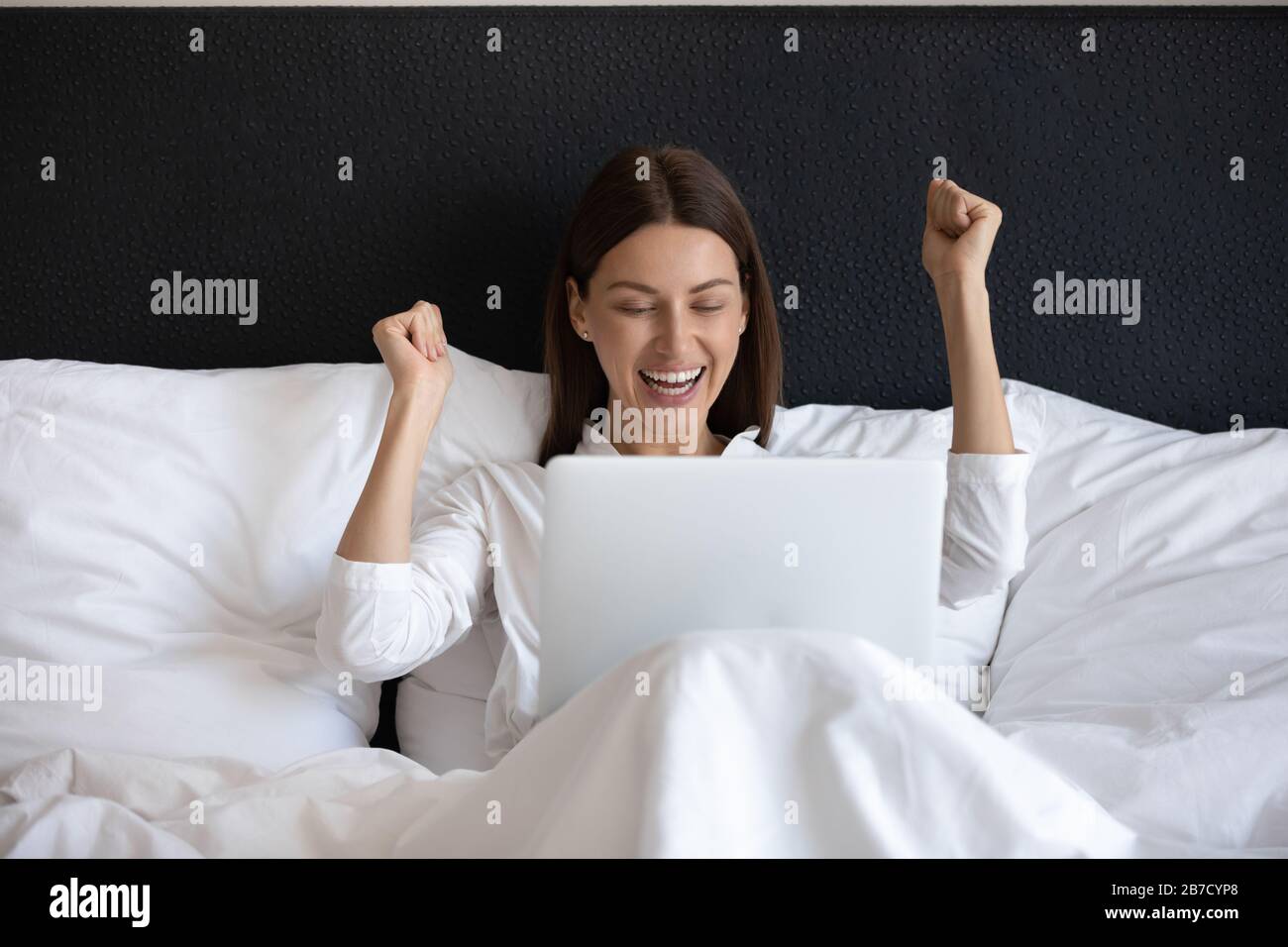 Giovane donna entusiasta che guarda lo schermo del notebook, che si rilassa a letto. Foto Stock