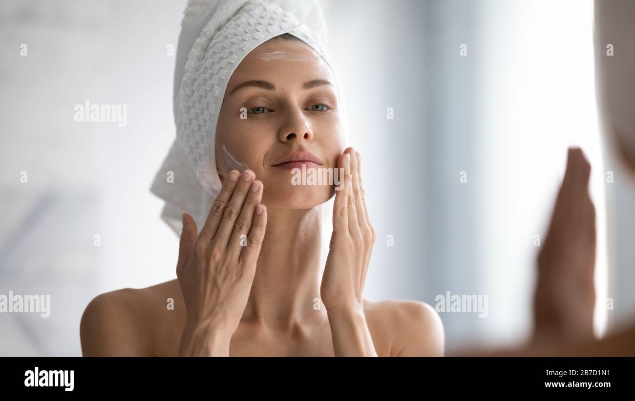 Sorridente giovane bella donna avvolta in asciugamano lisciare la pelle perfezionante. Foto Stock