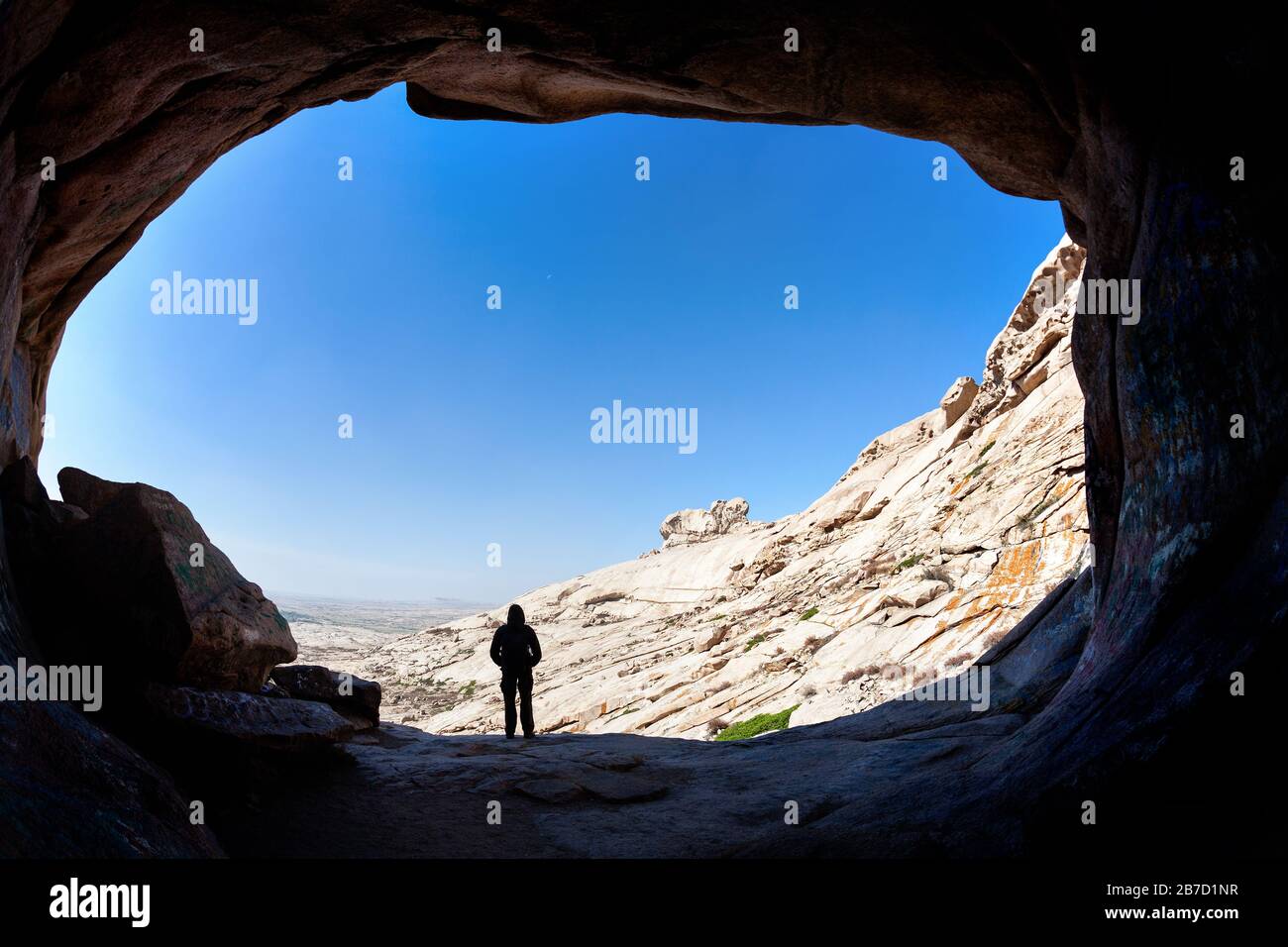 Uomo silhouette in piedi di fronte a un ingresso grotta nella montagna deserto del Kazakistan orientale Foto Stock