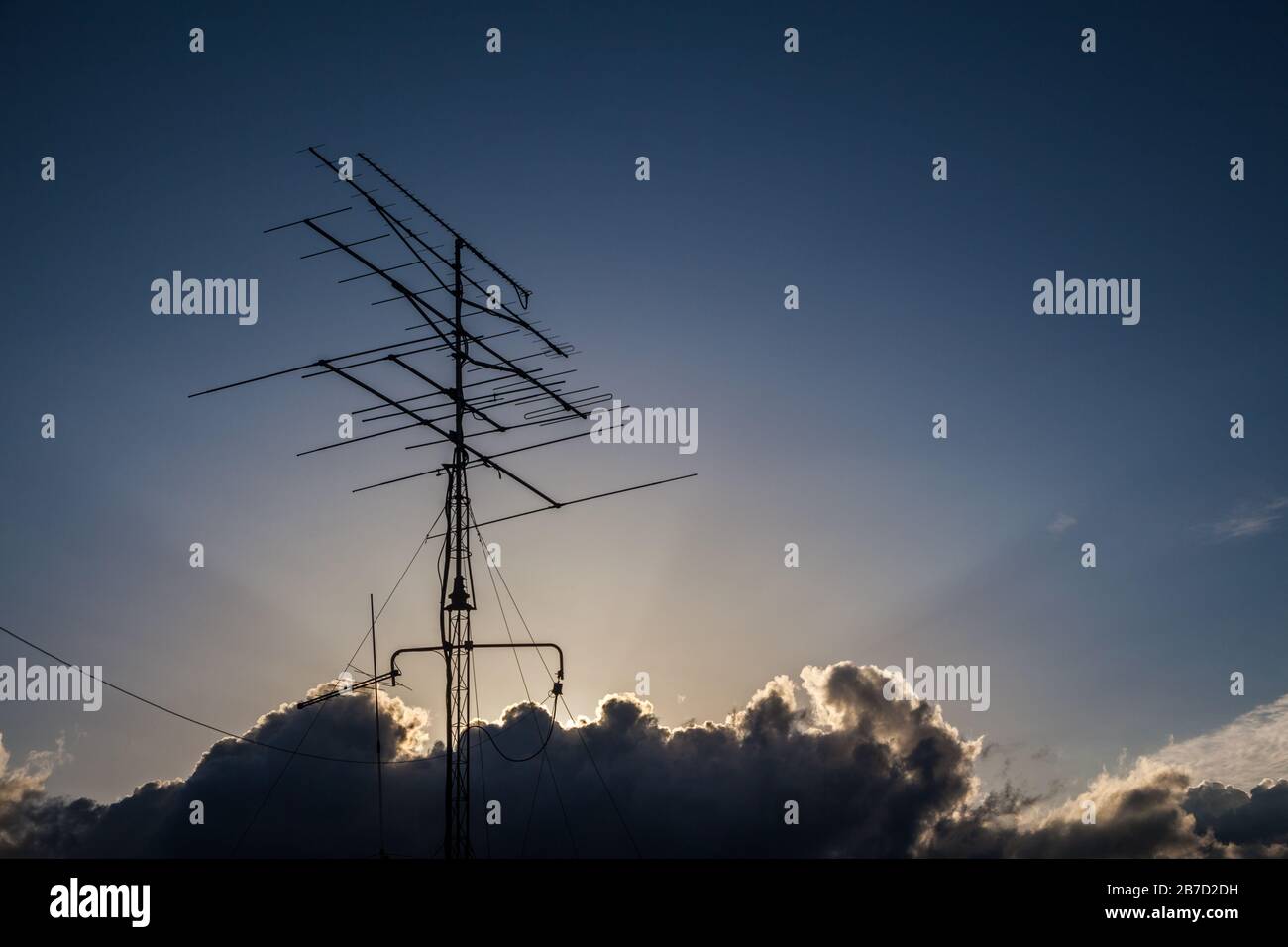 Sunbeams tra le nuvole nel cielo blu sopra un'antenna Foto Stock