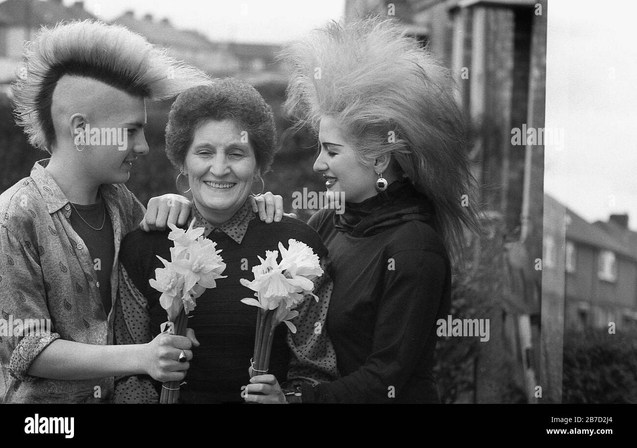 Anni '80, storico, Happy Mothers Day, due bambini nel 'goth' o 'punk' moda capelli del giorno, presentare la loro madre con i fiori, Inghilterra, Regno Unito. Foto Stock