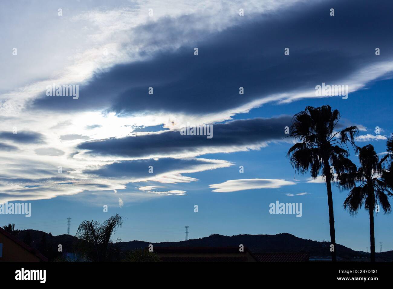 Silhouette di torri ad alta tensione e palme su blu cielo con nuvole bianche Foto Stock