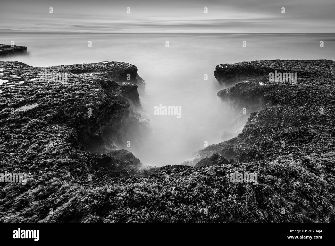 Una bella stagione in bianco e nero a tarda sera con rocce in primo piano, fotografata in un giorno tempestoso dopo il tramonto ad Arniston, Sud Africa. Foto Stock