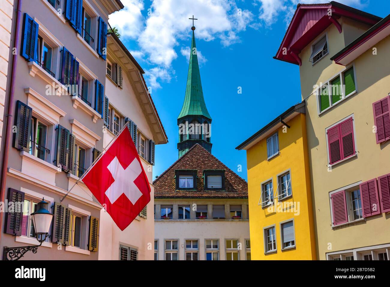 Bandiera svizzera ondeggiante, chiesa e facciate colorate di case nel centro storico di Zurigo, la più grande città della Svizzera in giornata di sole. Foto Stock