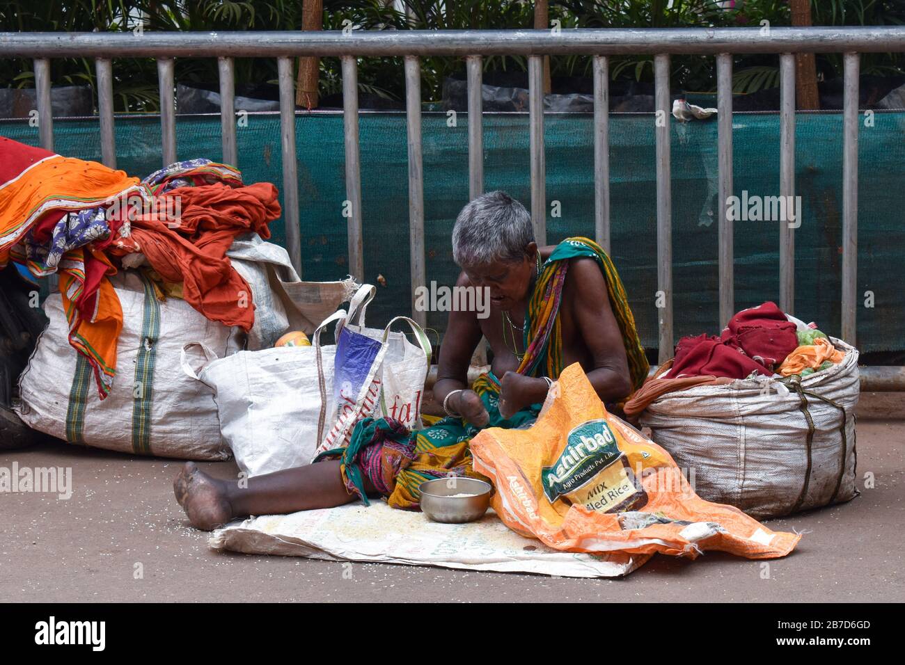 Un mendicante femminile handicappato con vestiti minimi seduti sulla strada cercando di gestire i suoi effetti personali vicino al Tempio di Jagannath, Puri, India Foto Stock