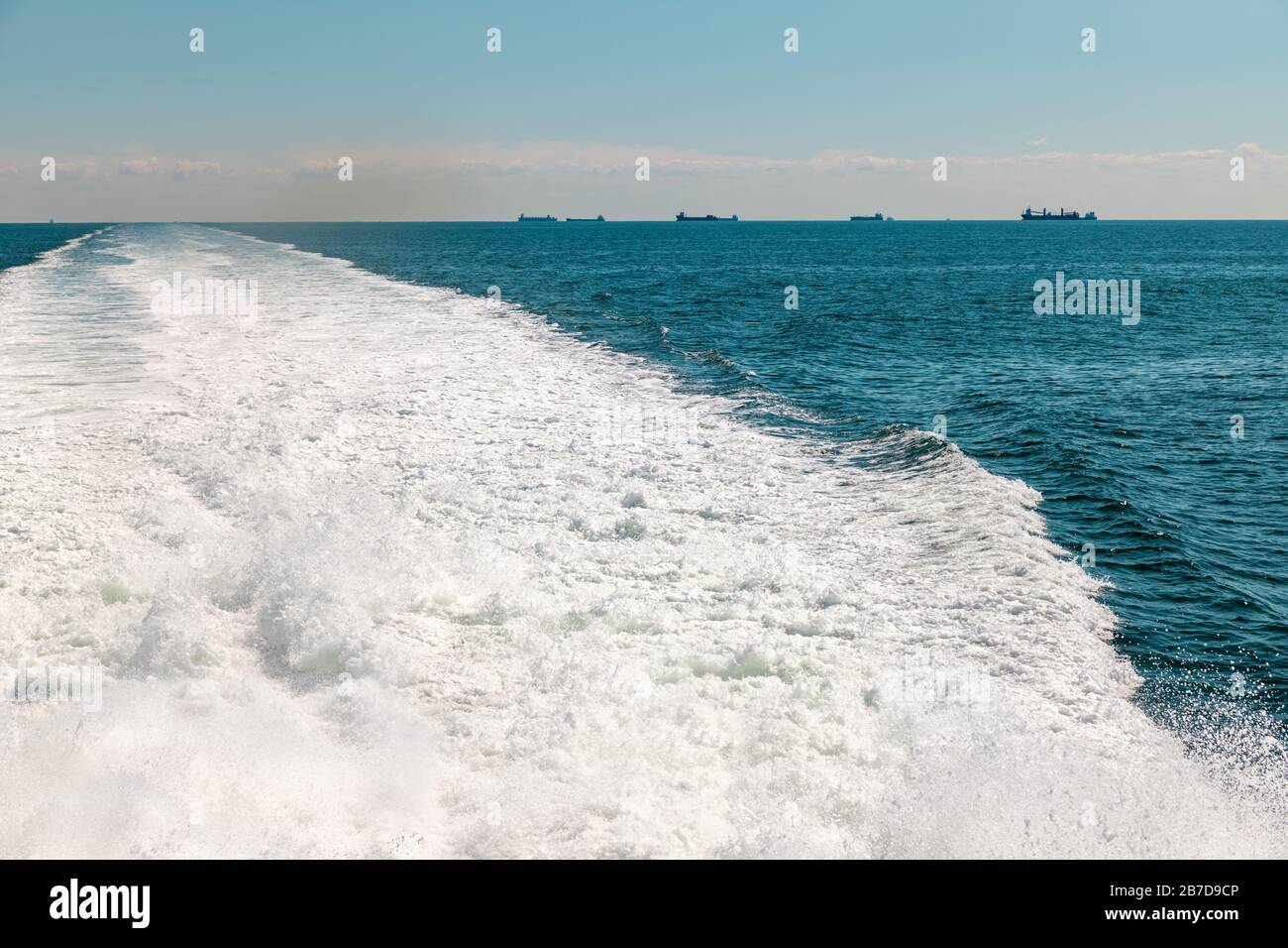 Barca veloce a vela in mare, sentiero dietro barca in acqua. Cielo blu senza nuvole, orizzonte chiaro. Foto Stock