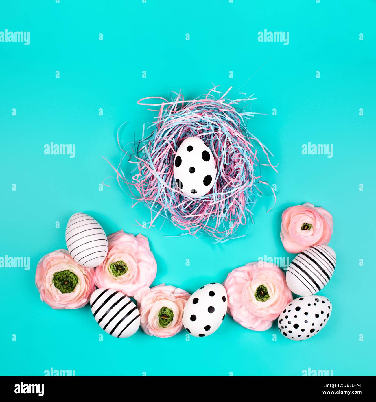 Nido d'uccello decorativo con uova grafiche creative e fiori ranunculus su sfondo blu pastello. Concetto di Pasqua. Foto Stock