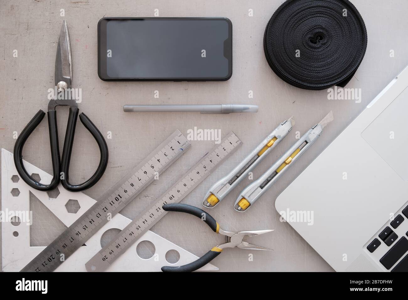 Area di lavoro di progettazione tecnica o industriale, vista dall'alto. Piatto con computer portatile, smartphone, corda, forbici, righelli e coltelli con grunge posteriore Foto Stock
