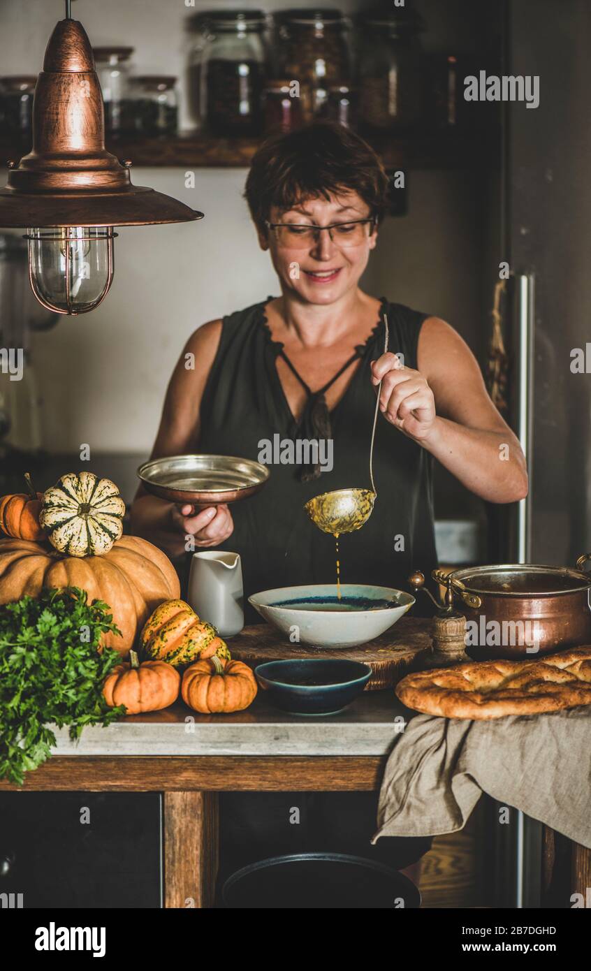 Eldery donna in abito scuro che serve stagionale autunno Crema di zucca zuppa in cucina moderna con interni. Stagionale autunno comfort food Foto Stock