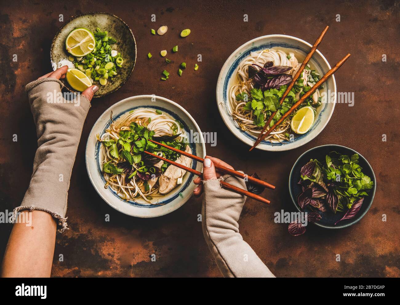 Pranzo di cucina Asiatica. Piatto di riso vietnamita noodle zuppa di pollo Pho Ga con coriandolo, germogli di soia, verdi in ciotola e mani donna con bacchette Foto Stock