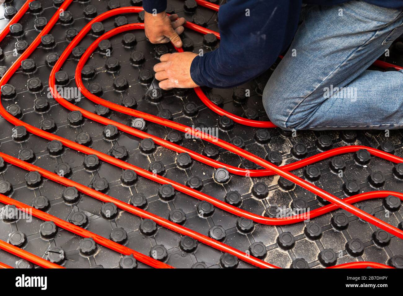 Lavoratore che installa tubi di impianto di riscaldamento a pavimento radiante Foto Stock