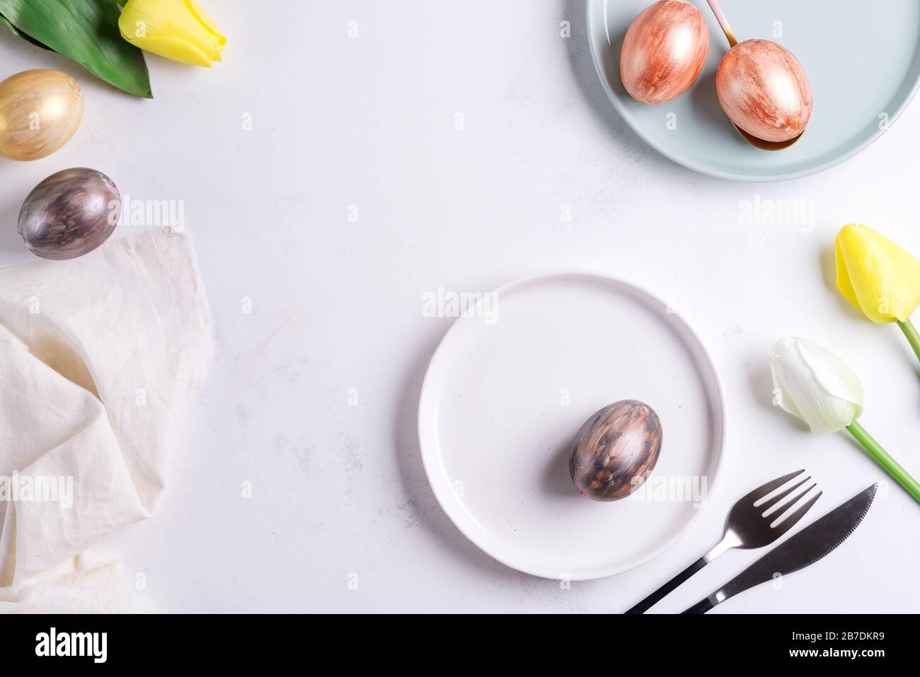 Tavola di Pasqua con tulipani di primavera. Elegante piatto vuoto, posate, tovagliolo e uova dorate su pietra Foto Stock