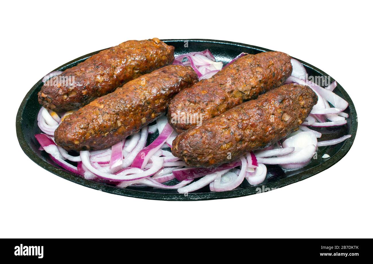 Kofta kebab e cipolle rosse su un piatto caldo sfrigolante su uno sfondo bianco isolato con un percorso di taglio Foto Stock