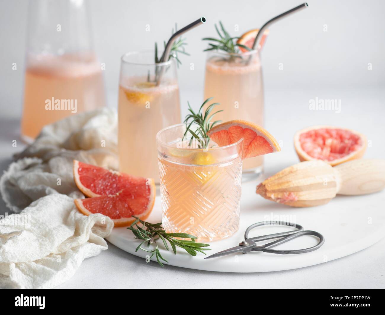 3 bicchieri di cocktail di pompelmo su vassoio di marmo con fette di rosmarino e pompelmo, caraffa e napkin mousseline Foto Stock