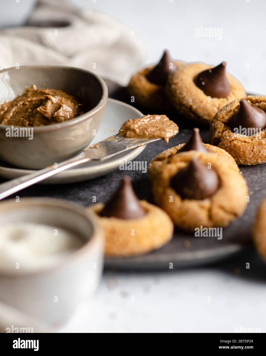 Burro di arachidi in una ciotola di presa su un piatto grigio scuro circondato da biscotti di baci di cioccolato Foto Stock